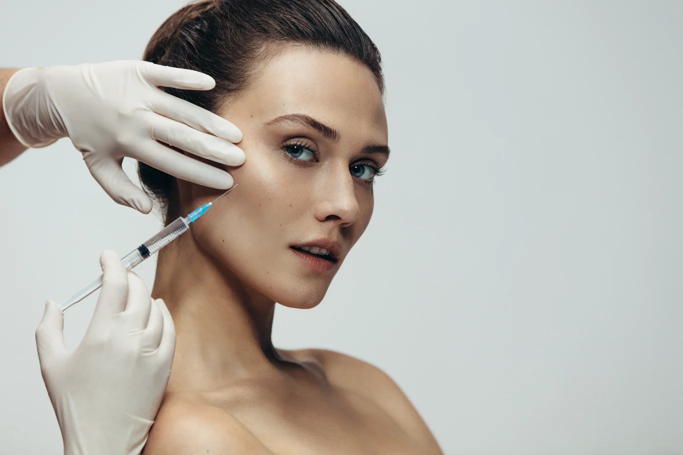 A close up of a woman receiving a precise cosmetic injection into her cheekbone area from a professional